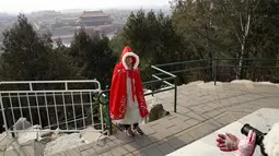 Seorang pengunjung berfoto dengan pemandangan menghadap Kota Terlarang dari taman Jingshan pada hari bersalju di Beijing, China, Selasa (19/1/2021). China sekarang berurusan dengan pandemi virus corona di timur lautnya yang mendorong penguncian ketat dan pembatasan perjalanan. (AP Photo/Ng Han Guan)