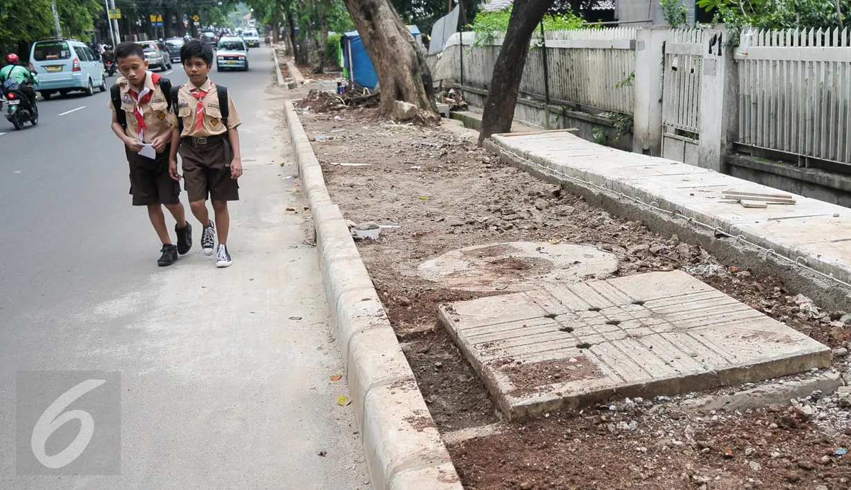 Dua pelajar melintas di samping lokasi pembangunan trotoar di Jalan Raya Ragunan, Jakarta, Rabu (12/10). Suku Dinas Bina Marga Jaksel menganggarkan Rp79 miliar untuk pembangunan dan perbaikan trotoar di 10 kecamatan Jaksel. (Liputan6.com/Yoppy Renato)