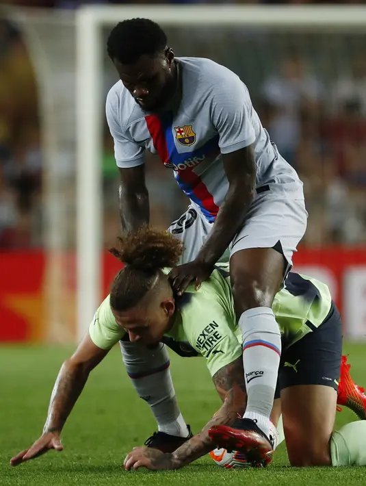 Gelandang Manchester City Kalvin Phillips berebut bola dengan gelandang Barcelona Franck Kessie pada sebuah laga amal di Stadion Camp Nou, Kamis (25/8/2022) dini hari WIB. Laga Barcelona vs Man City berjalan ketat, skor akhir sama kuat 3-3. (AP Photo/Joan Monfort)