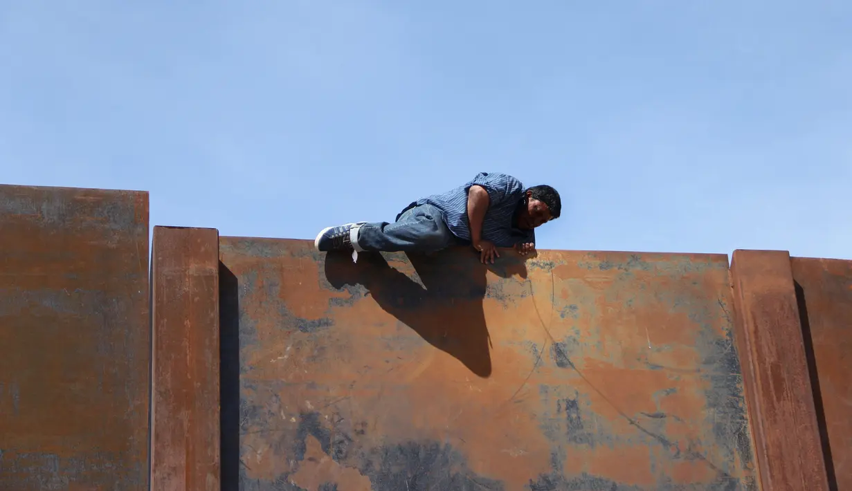 Seorang pemuda memanjat tembok besi perbatasan antara Meksiko dan Amerika Serikat di negara bagian Chihuahua, Meksiko (6/4). Mereka menyeberang secara ilegal ke Sunland Park dari Ciudad Juarez. (AFP/Herika Matinez)