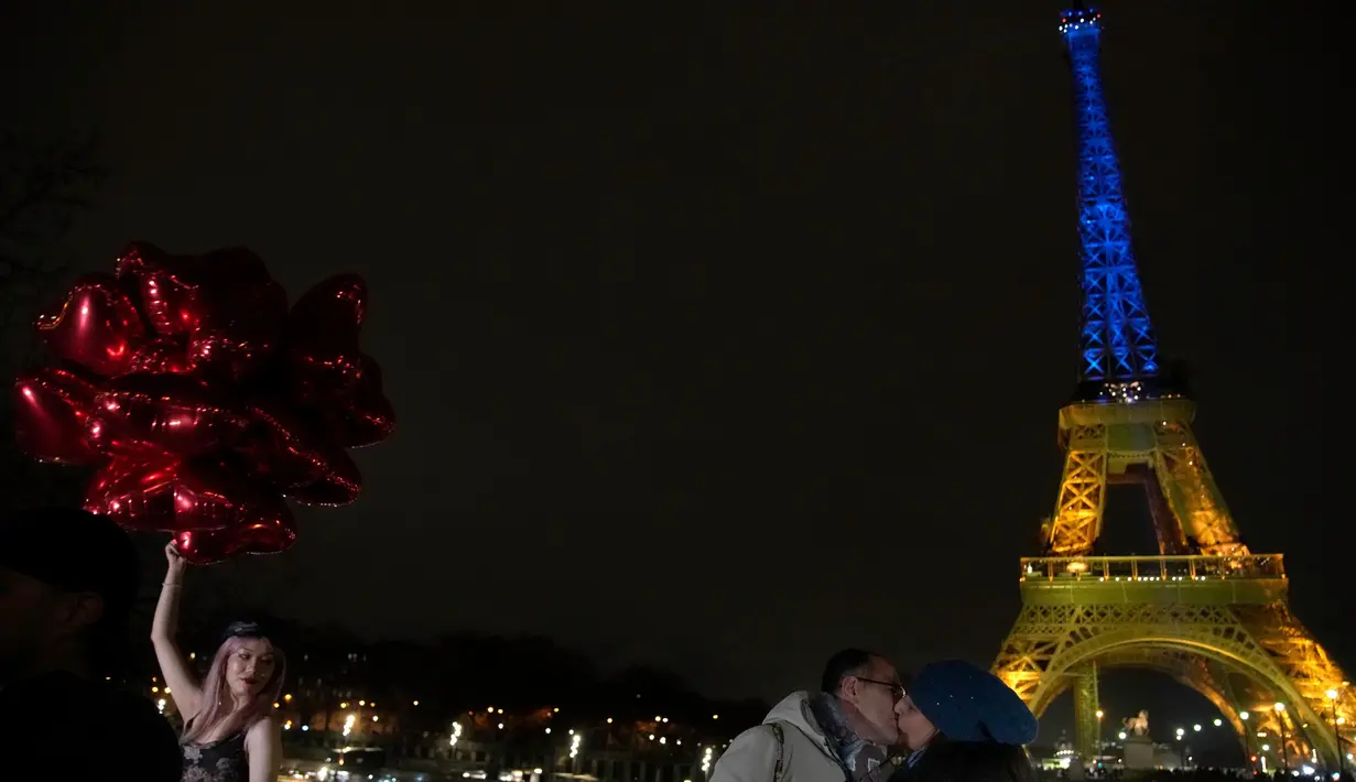 Para turis berpose dengan balon saat Menara Eiffel diterangi dengan warna-warna khas Ukraina untuk menandai peringatan satu tahun invasi Rusia ke negara tersebut, di Paris, Kamis, 23 Januari 2023. Pada 24 Februari 2022 lalu Rusia menginvasi Ukraina dan menandai puncak eskalasi konflik kedua negara sejak 2014 silam. (AP Photo/Christophe Ena)