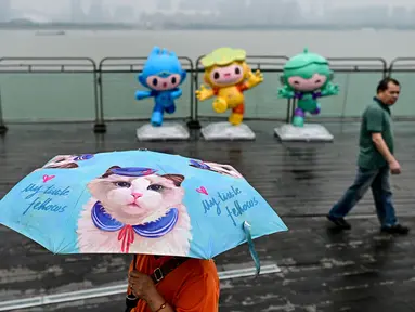 Seorang pejalan kaki menggunakan payung saat melintas di pedestrian Sungai Qiantang. Hangzhou, Zhejiang, China yang berhias maskot Asian Games 2022 (Chenchen, Congcong, dan Lianlian) pada 22 September 2023 waktu setempat. (AFP/Manan Vatsyayana)