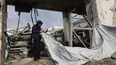 Warga Palestina di Gaza terpaksa bertahan di tenda-tenda yang rusak atau rumah-rumah yang tidak layak huni karena proses pembangunan kembali terhambat. Tampak dalam foto, seorang pria Palestina memperbaiki tenda perlindungan di sebuah bangunan yang rusak akibat perang, dimana sebagian bangunan tersebut runtuh pada hari musim dingin yang berangin di Kota Gaza pada Selasa 13 Januari 2026. (Omar AL-QATTAA/AFP)
