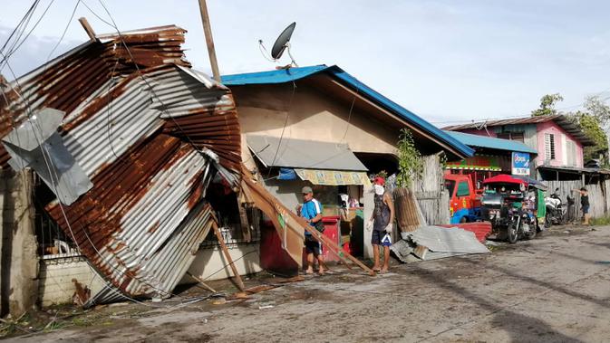 Warga berdiri dekat sebuah rumah yang rusak akibat terjangan topan Phanfone yang menerjang Ormoc City, Provinsi Leyte, Filipina, Rabu (25/12/2019). Topan membuat jutaan warga di negara yang mayoritas beragama Katolik itu merayakan Natal dengan kesedihan. (RONALD FRANK DEJON/AFP)