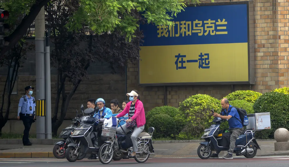 Seorang polisi berpatroli ketika orang-orang yang mengendarai sepeda dan skuter menunggu untuk menyeberangi persimpangan dekat tanda bertuliskan "Kami mendukung Ukraina" di luar Kedutaan Besar Kanada di Beijing, China, Rabu (17/5/2023). (AP Photo/Mark Schiefelbein)