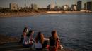 Sejumlah wanita mengenakan masker duduk di depan laut di Barcelona, Spanyol, Rabu, (20/5/2020). Berjemur dan berenang masih tidak diizinkan di pantai tersebut.  (AP Photo/Emilio Morenatti)