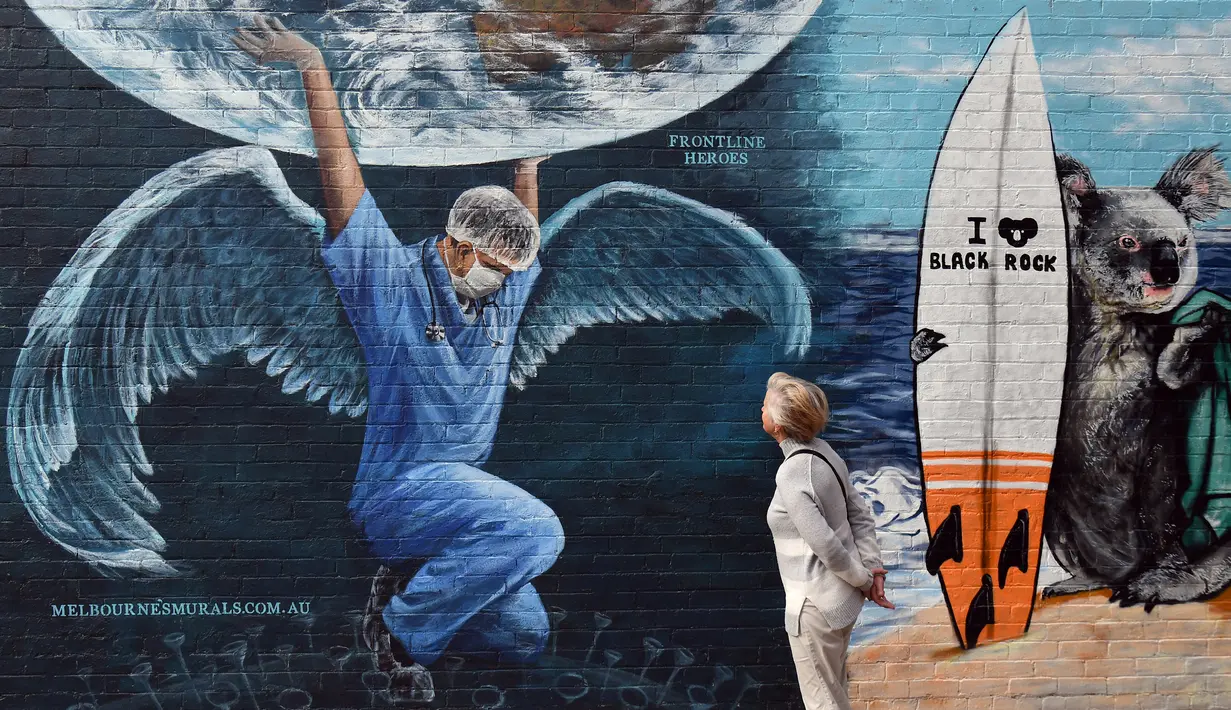 Seorang wanita memandangi mural yang menggambarkan petugas kesehatan dengan sayap memegang bola dunia pada Hari Perawat Internasional di Melbourne,Australia, Selasa (12/5/2020). Petugas medis menghadapi risiko besar di tengah pandemi virus corona COVID-19 seperti sekarang ini. (William WEST/AFP)