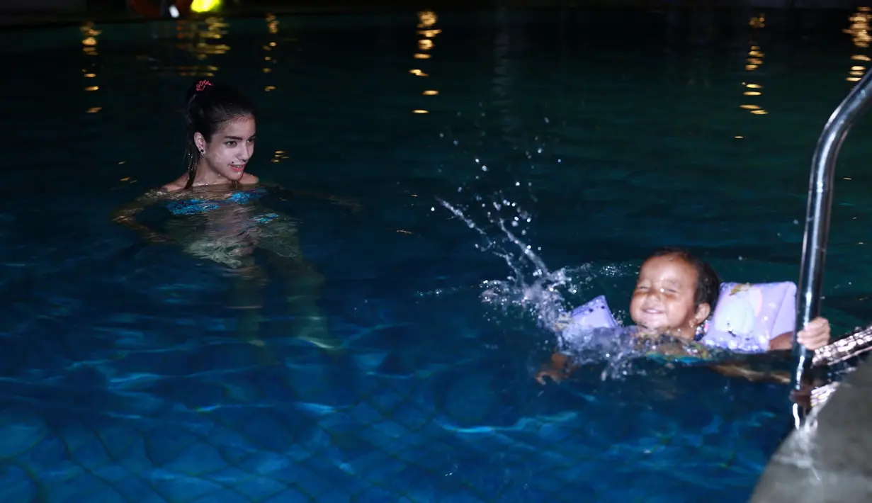 Setelah menemani anaknya bermain di playground, ibu tiga anak itu langsung membawa buah hatinya ke Nusa Dua Beach, Bali. Di sana, mereka merasakan sensasi berenang di malam hari. (Galih W. Satria/Bintang.com)
