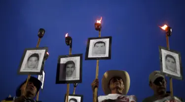 Kerabat membawa obor dan poster bergambar wajah 43 mahasiswa yang menghilang, ketika long march di jalanan Meksiko City, Selasa (26/4). Mereka mendesak pemerintah segera menangani kasus yang sudah 19 bulan berlalu tersebut. (REUTERS/Edgard Garrido)