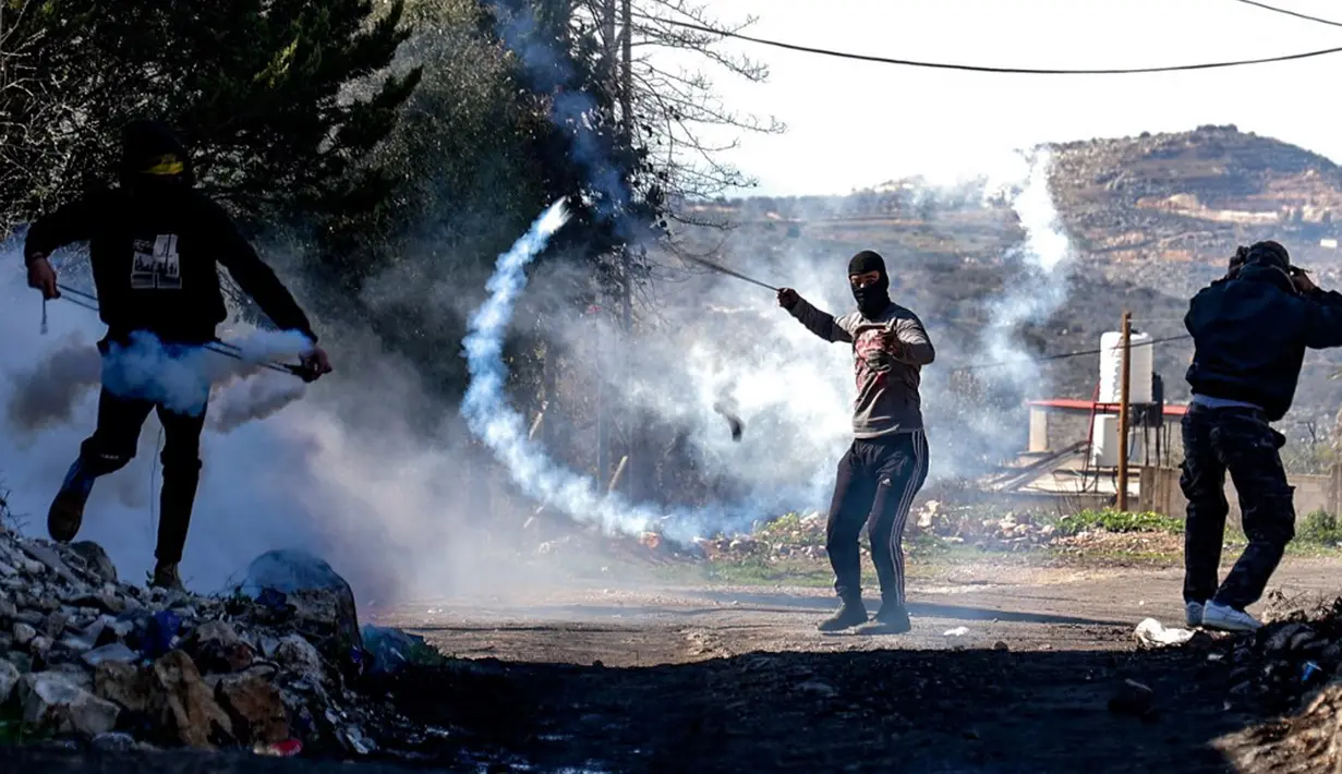 Seorang pemuda Palestina menggunakan ketapel untuk mengembalikan tabung gas air mata ke arah pasukan keamanan Israel saat bentrok pada demonstrasi menentang pengambilalihan tanah oleh Israel dekat pemukiman Yahudi Kedumim di Desa Kfar Qaddum, Tepi Barat, 21 Januari 2022. (JAAFAR ASHTIYEH/AFP)