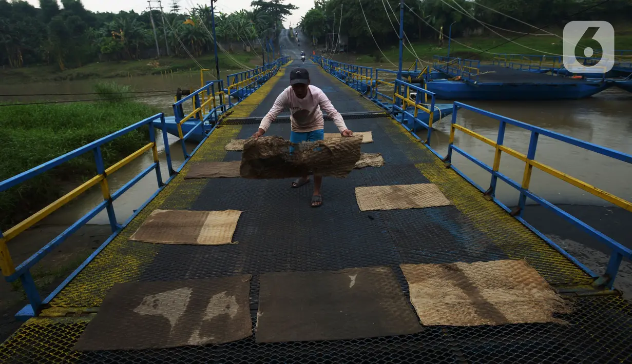 Warga menaruh kain pada jembatan perahu di atas Sungai Citarum, Karawang, Jawa Barat, Sabtu (20/11/2021). Jembatan perahu ini menjadi jalan alternatif yang menghubungkan antara Desa Anggadita dengan Kawasan Pabrik Dusun Rumambe 1. (merdeka.com/Imam Buhori)