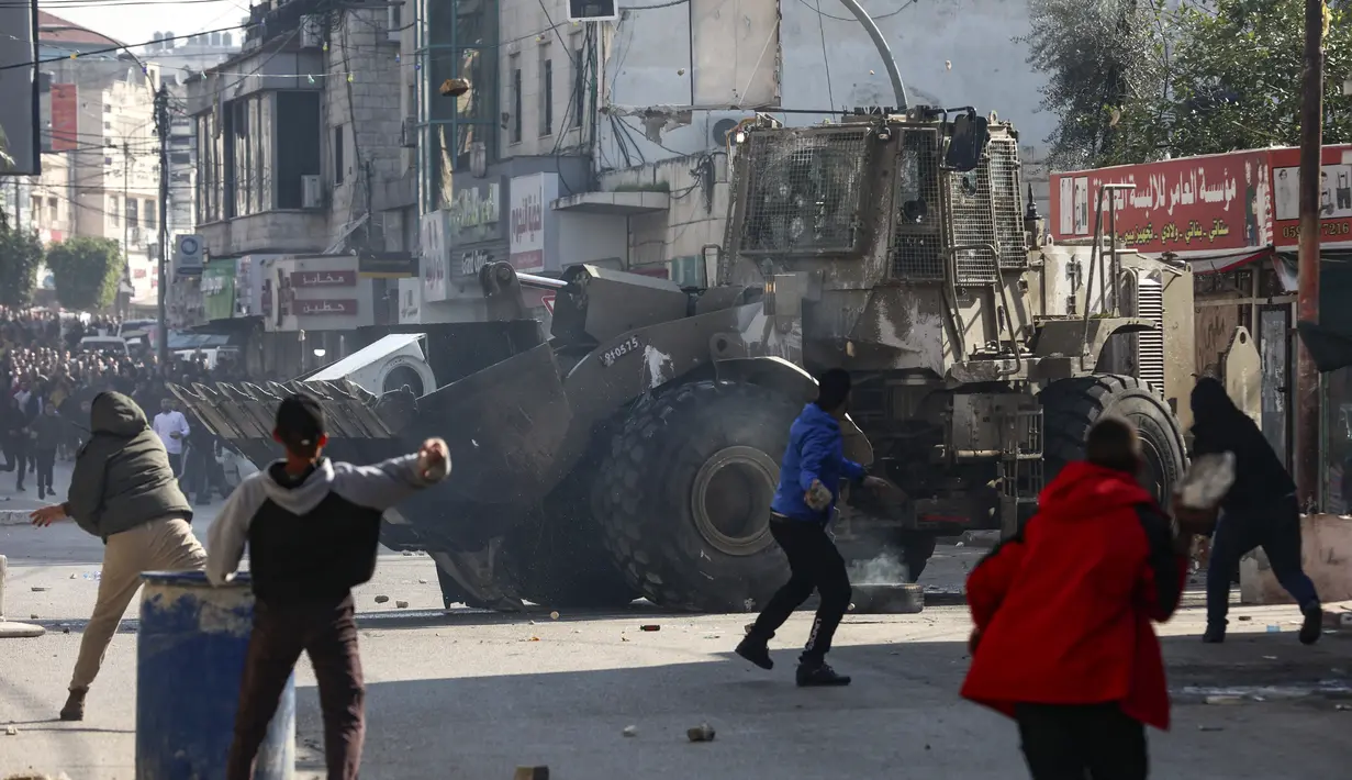 Warga Palestina melemparkan batu ke buldoser tentara Israel, selama konfrontasi di kota Jenin di Tepi Barat yang diduduki, pada 26 Januari 2023. Serangan Israel di kamp pengungsi Jenin di Tepi Barat hari ini menewaskan 9 warga Palestina termasuk seorang wanita lanjut usia, kata pejabat Palestina. (AFP/Jaafar Ashtiyeh)