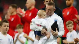 Striker Inggris, Wayne Rooney meggendong anaknya sebelum pertandingan persahabatan melawan Amerika Serikat (AS) di Stadion Wembley, Inggris (16/11). Wayne Rooney merupakan pencetak gol terbanyak di Timnas Inggris. (AFP Photo/Ian Kington)
