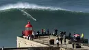Orang-orang di atas mercusuar menyaksikan peselancar menunggangi ombak selama sesi selancar derek di Praia do Norte atau Pantai Utara di Nazare, Portugal, Kamis (29/10/2020). (AP Photo/Pedro Rocha)