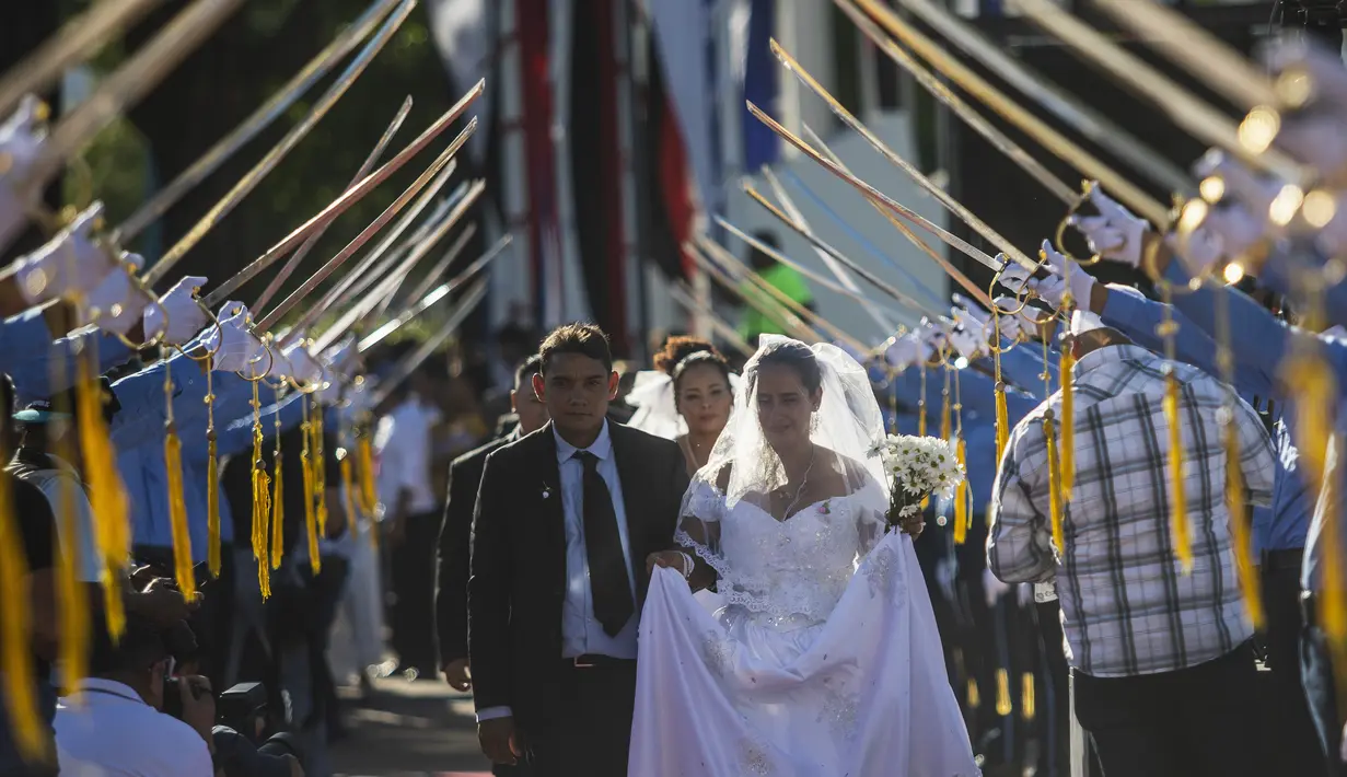 Pasangan berjalan di bawah penjaga kehormatan pedang kadet polisi saat pernikahan massal pada Hari Valentine di Managua, Nikaragua, Selasa (14/2/2023). Acara tersebut diselenggarakan oleh stasiun radio Sandinista "La Nueva Radio Ya", dan sekitar 263 pasangan menikah di Lapangan Revolusi. (AP Photo/Inti Ocon)