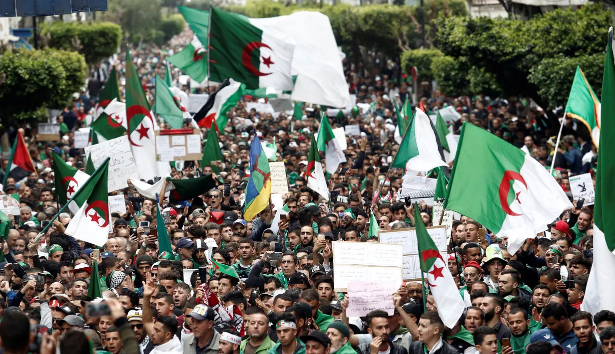 Demonstran memegang bendera dan spanduk saat berunjuk rasa di Aljir, Aljazair, Jumat (19/4). Demonstran kembali turun ke jalan-jalan untuk mendesak perubahan demokrasi besar-besaran melampaui pengunduran diri mantan presiden Abdelaziz Bouteflika. (REUTERS/Ramzi Boudina)