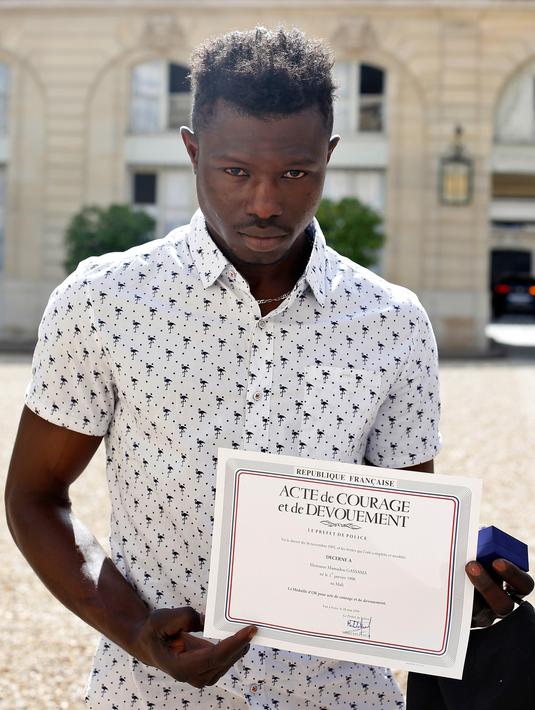 Imigran asal Mali, Mamoudou Gassama menunjukkan sertifikat penghargaan di Paris, Prancis, Senin (29/5). Gassama mendapat penghargaan setelah memanjat gedung apartemen untuk menyelamatkan balita yang hampir jatuh. (AP Photo/Thibault Camus, Pool)