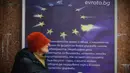 Mengadopsi euro dinilai sebagai fase akhir integrasi Bulgaria ke arus utama Eropa, setelah bergabung dengan NATO, Uni Eropa, kawasan Schengen, dan kini zona mata uang tunggal. Tampak dalam foto, seorang wanita berjalan melewati poster yang menampilkan Bulgaria sebagai anggota Zona Euro ke-21, di Sofia, Kamis 1 Januari 2026, saat negara tersebut bergabung dengan serikat mata uang euro. (AP Photo/Valentina Petrova)