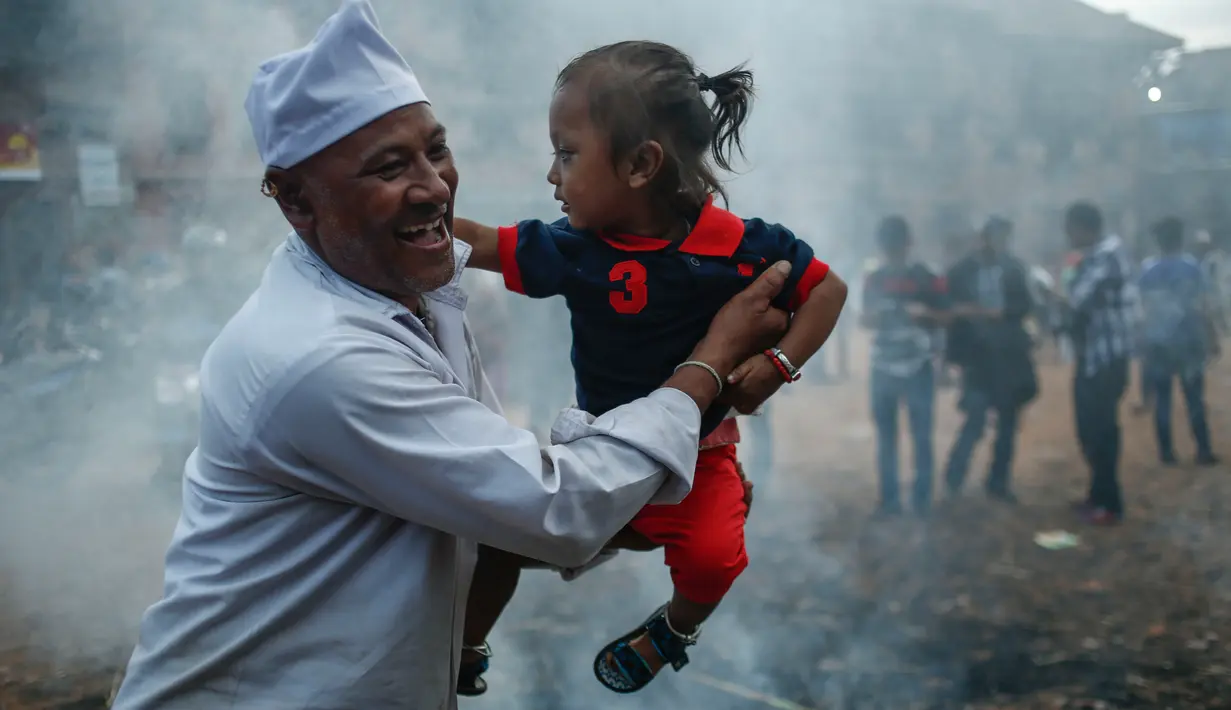 Seorang pria membawa anaknya ke dekat api bekas pembakaran patung jerami dalam perayaan Ghanta Karna di Bhaktapur di pinggiran Kathmandu, Nepal (21/7). (AFP Photo/Uma Bista)