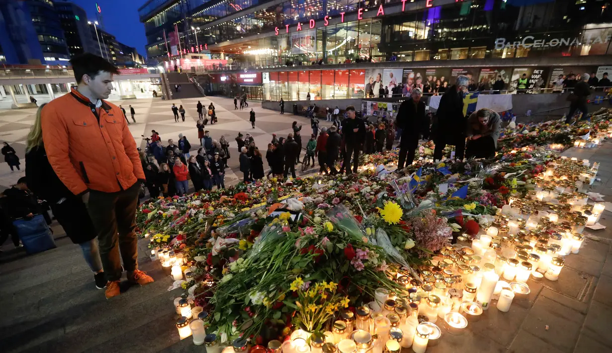 Seorang pria melihat lilin dan bunga yang diletakkan di lokasi terjadinya serangan truk di Stockholm, Swedia, Minggu (9/4). Sebuah truk yang dibajak menabrakkan diri ke kerumunan pejalan kaki pada Sabtu (8/4). (AP Photo / Markus Schreiber)