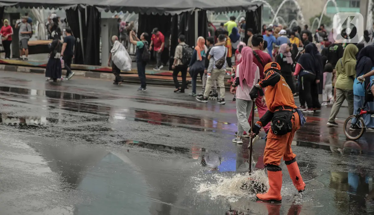 Petugas Penanganan Prasaran dan Sarana Umum (PPSU) membersihkan genangan air saat car free day (CFD) di kawasan Bundaran HI, Jakarta, Minggu (29/12/2019). Pembersihan genangan air dilakukan agar warga yang sedang berolahraga di kawasan tersebut nyaman. (Liputan6.com/Faizal Fanani)