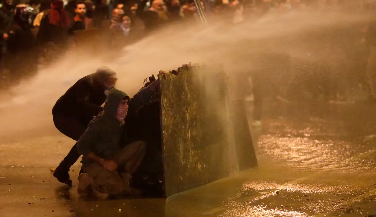 Demonstran antipemerintah berlindung dari semprotan air saat bentrok dengan polisi antihuru-hara dalam demonstrasi menentang pemerintahan baru dekat Parliament Square, Beirut, Lebanon, Rabu (22/1/2020). AP Photo/Hussein Malla)