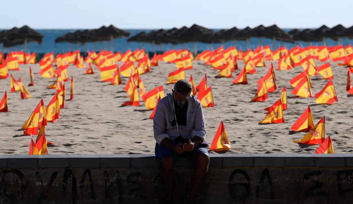 Seorang pria duduk di dekat ribuan bendera Spanyol yang mewakili korban COVID-19 di negara itu dipasang di pantai Patacona, Valencia pada Minggu (4/10/2020). Virus corona di Spanyol sejauh ini telah merenggut lebih dari 32.000 nyawa dan 790.000 kasus terkonfirmasi. (Jose Jordan / AFP)