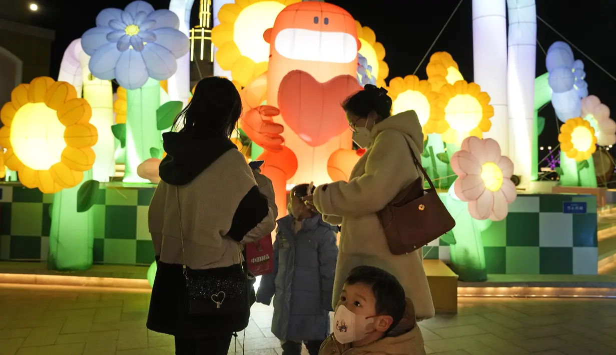 Seorang anak bermasker berdiri di dekat dekorasi lampu di sebuah mal di Beijing, Jumat, 30 Desember 2022. Strategi "nol-Covid" mengurung jutaan keluarga di rumah mereka selama berminggu-minggu, menutup sebagian besar perjalanan masuk dan keluar China, dan mengosongkan jalan-jalan ramai di kota-kota besar. (AP Photo/Ng Han Guan)