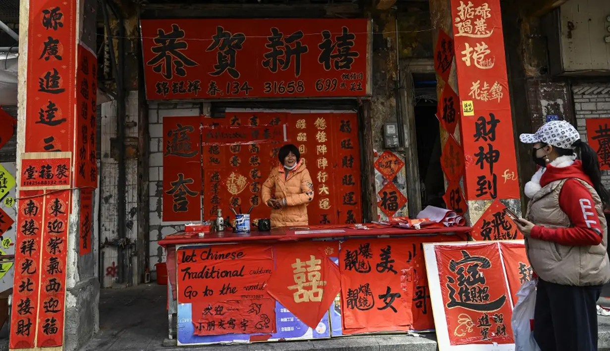 Seorang penjual menjual kuplet musim semi, semacam dekorasi Tahun Baru Imlek, jelang dimulainya Tahun Baru Imlek di sebuah kios di Foshan, Provinsi Guangdong, China, 18 Januari. Angka dua pada kuplet merupakan angka genap yang dikaitkan dengan keberuntungan dalam budaya China. (Giok Gao/AFP)