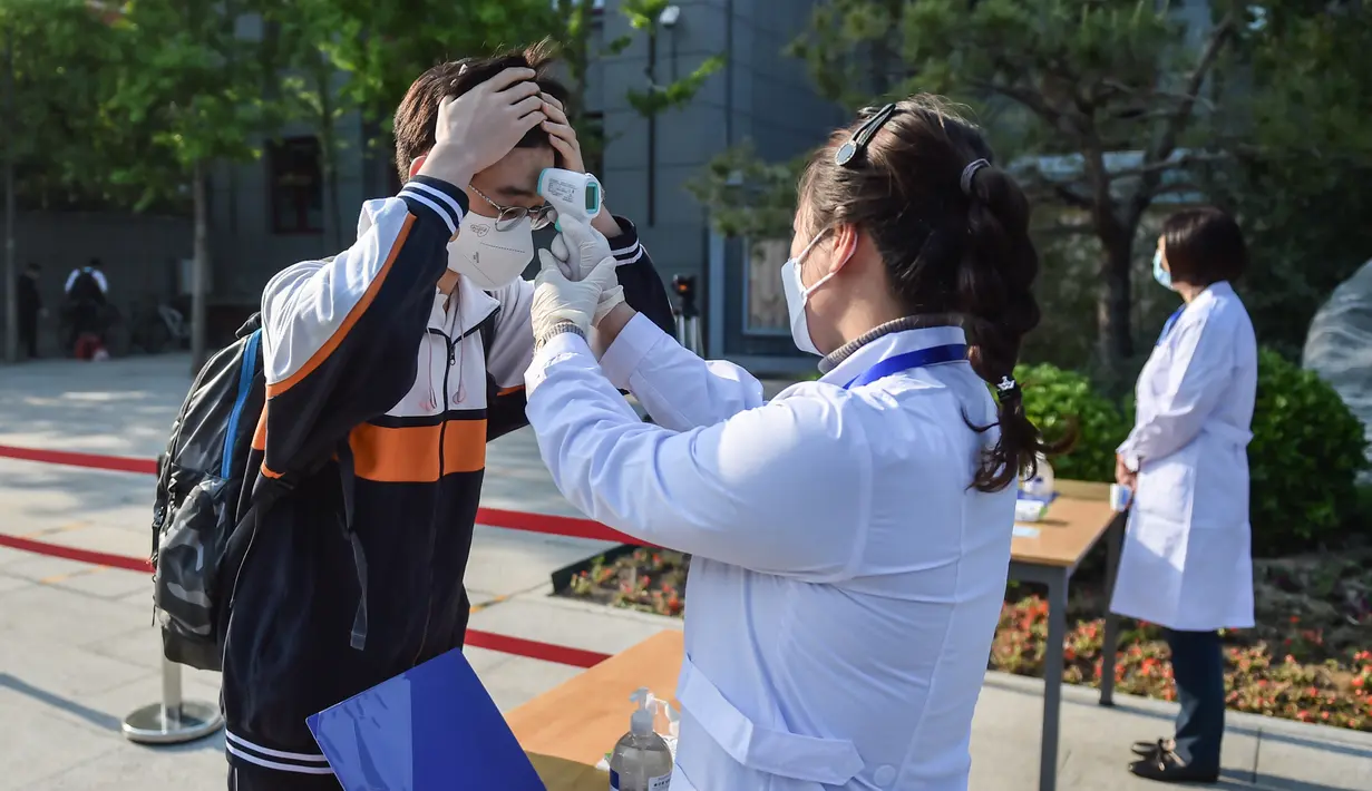 Staf mengukur suhu tubuh seorang siswa di Sekolah Menengah Atas No. 161 Beijing, Beijing, China, Senin (27/4/2020). Sekolah menengah atas di Beijing memulai kembali kegiatan belajar di kelas untuk siswa tingkat akhir yang akan mengikuti ujian masuk perguruan tinggi. (Xinhua/Peng Ziyang)
