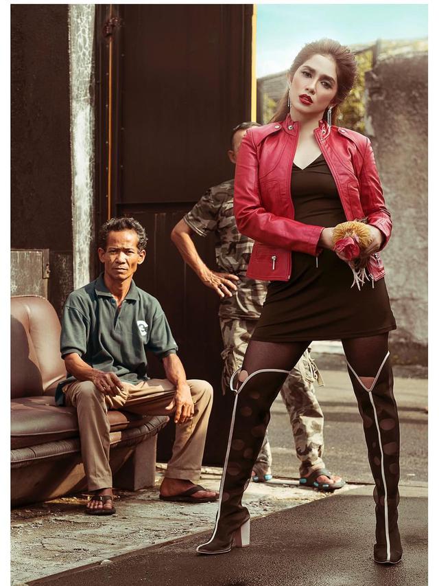 Ussy bergaya di depan warga di gang yang sempit sambil memegang ayam jago.