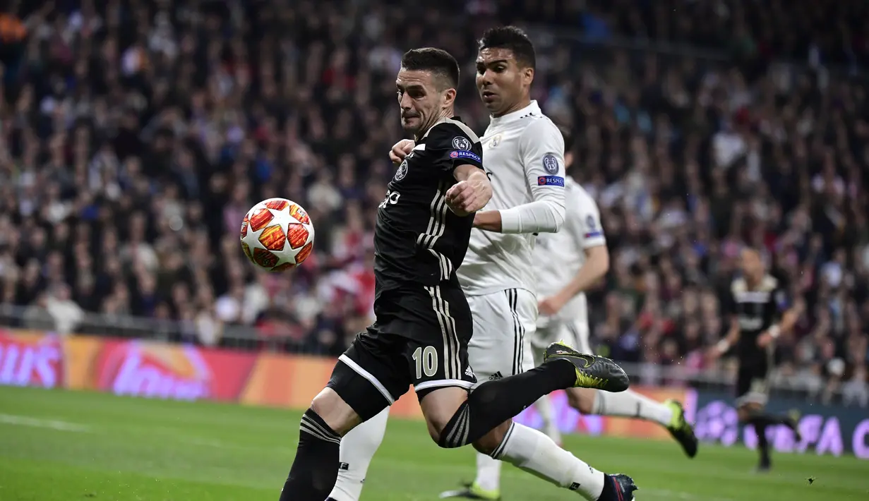 Gelandang Ajax, Dusan Tadic mencoba melewati Casemiro pada laga leg kedua, babak 16 besar Liga Champions yang berlangsung di Stadion Santiago Bernabeu, Madrid, Rabu (6/3). Real Madrid kalah 1-4 kontra Ajax. (AFP/Gabriel Bouys)