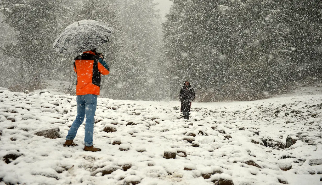 Turis India (kiri) mengambil foto selama hujan salju di Gulmarg, sekitar 55 km sebelah utara Srinagar, Kashmir, Selasa (3/1). Gelombang dingin yang melanda Kashmir kian parah hingga mencapai suhu di bawah nol derajat celcius. (Tauseef Mustafa/AFP)