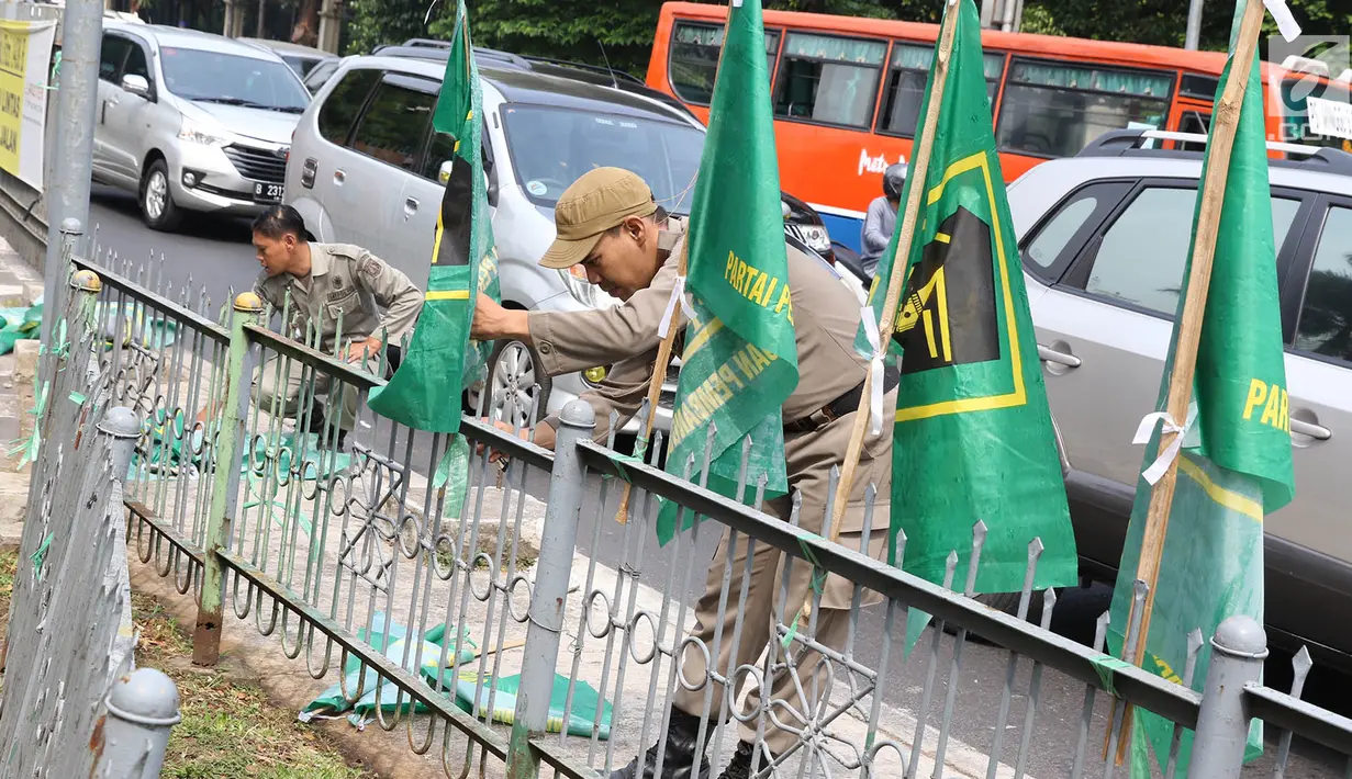 Petugas Satpol PP mencopot bendera partai politik di sepanjang pagar kawasan Pancoran, Jakarta. Selasa (18/7). Pencopotan dilakukan untuk menertibkan bendera partai politik liar yang memenuhi ruang publik di Ibukota. (Liputan6.com/Immanuel Antonius)
