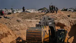 Warga Palestina menyaksikan aktivitas pekerja Mesir yang menggunakan alat berat untuk mencari jenazah para sandera di Kota Hamad, Khan Younis, di Jalur Gaza selatan, Selasa 28 Oktober 2025. Di Khan Younis, proses penggalian tanah terlihat menggunakan alat berat di tengah reruntuhan. (AP Photo/Abdel Kareem Hana)