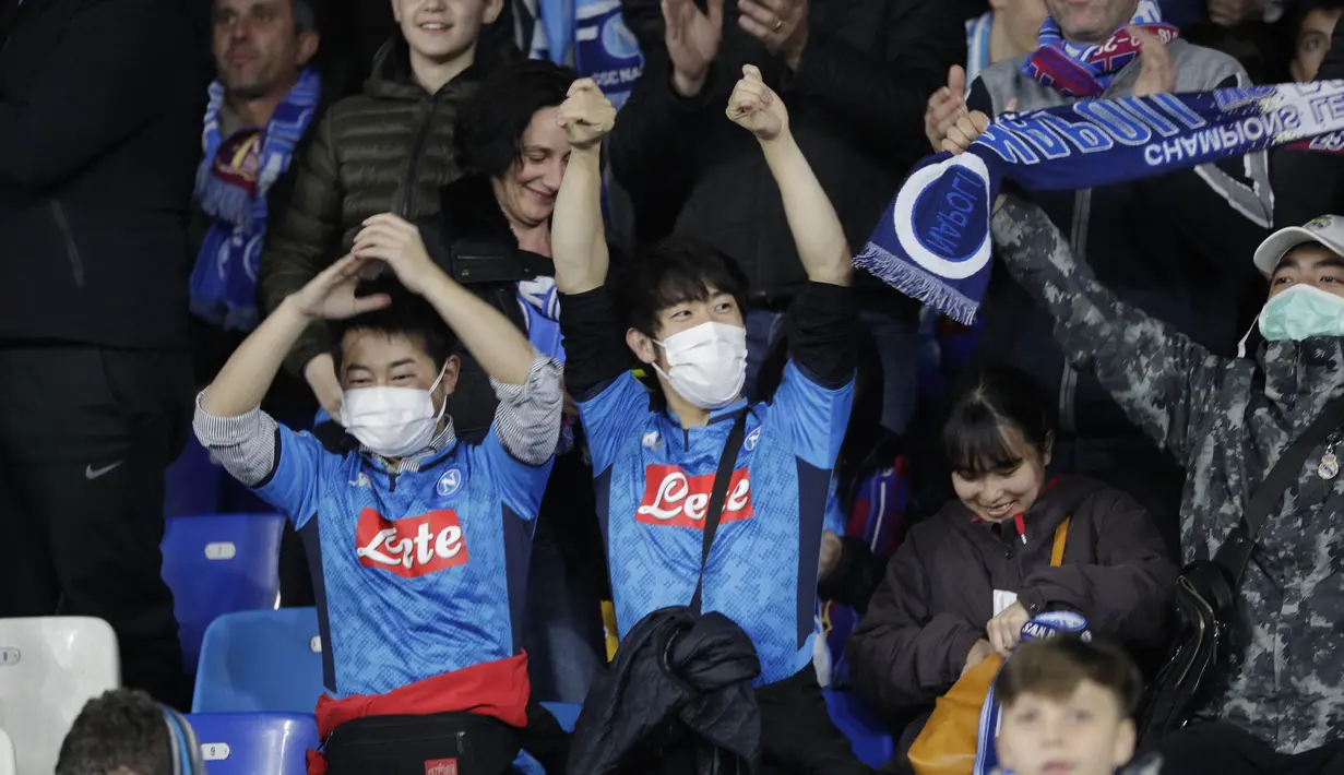 Dua suporter Napoli mengenakan masker menunggu dimulainya pertandingan antara Napoli dan Barcelona di Stadion San Paolo di Naples, Italia, Selasa, (25/2/2020). Italia melaporkan kenaikan kasus infeksi virus Corona COVID- 91 menjadi lebih 272 kasus. (AP Photo/Andrew Medichini)