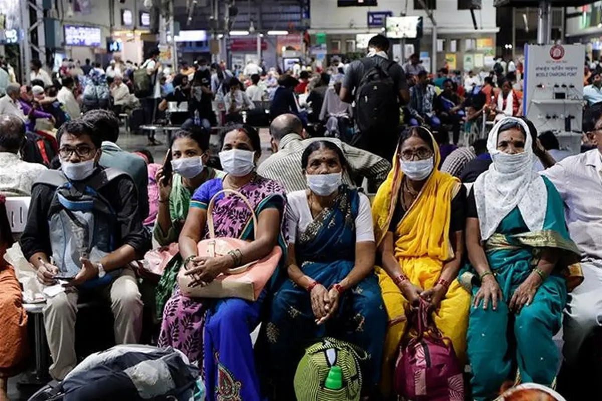 Orang India yang menunggu di stasiun kereta api memakai masker pelindung sebagai tindakan pencegahan terhadap pandemi Virus Corona.