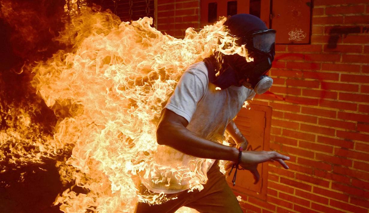 Seorang demonstran berlari saat tubuhnya terbakar disela unjuk rasa yang diwarnai bentrokan menentang Presiden Venezuela, Nicolas Maduro di Caracas, Rabu (3/5). Pria itu tersulut api dari ledakan tangki sepeda motor milik polisi. (RONALDO SCHEMIDT / AFP)