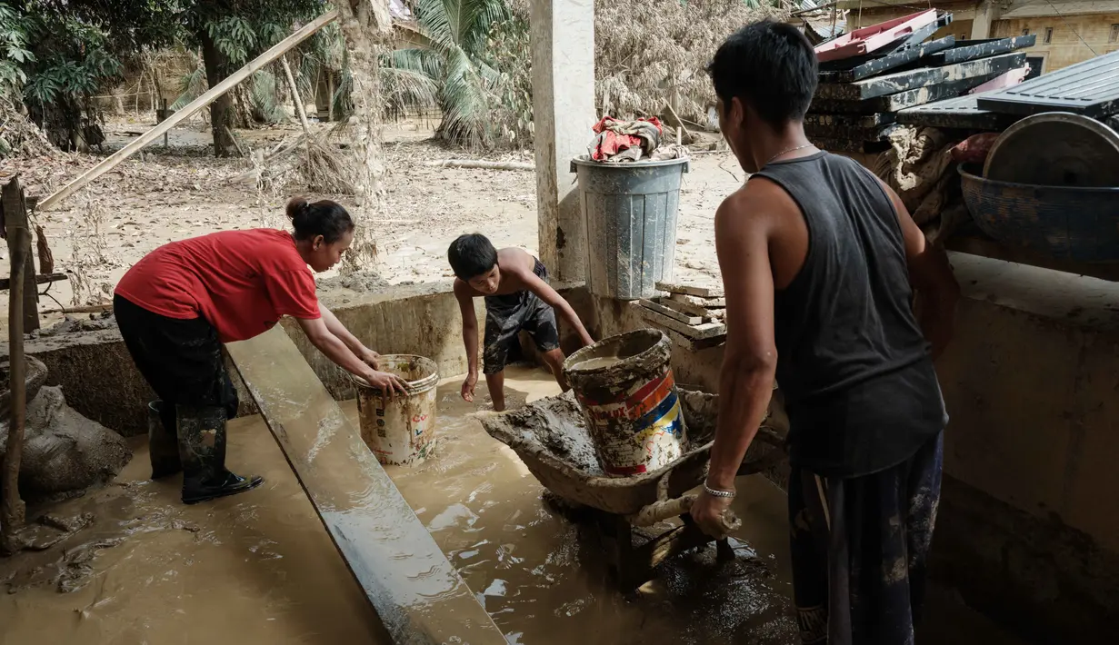 Pembersihan rumah dan barang-barang dilakukan agar mereka dapat segera kembali ke rumah setelah mengungsi. Tampak dalam foto, Panji (kanan), 23 tahun, membawa lumpur keluar dari dapur menggunakan gerobak dorong di rumah orang tuanya, setelah banjir bandang, di Aceh Tamiang, Minggu 14 Desember 2025. (Yasuyoshi CHIBA/AFP)