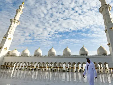 Seorang pria berjalan melewati halaman Masjid Agung Sheikh Zayed di Abu Dhabi, Uni Emirat Arab. Masjid ini adalah masjid terbesar ketiga di dunia setelah masjid di Mekkah dan Madinnah. (Photo by Vincenzo PINTO / AFP)