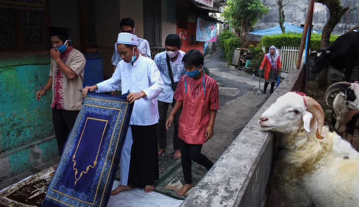 Umat ​​muslim bersiap melaksanakan salat Idul Adha di samping kambing kurban dekat masjid di Bandung, Jawa Barat, Selasa (20/7/2021). Umat muslim Indonesia melewati Hari Raya Idul Adha tahun ini di tengah gelombang virus corona COVID-19. (Timur Matahari/AFP)