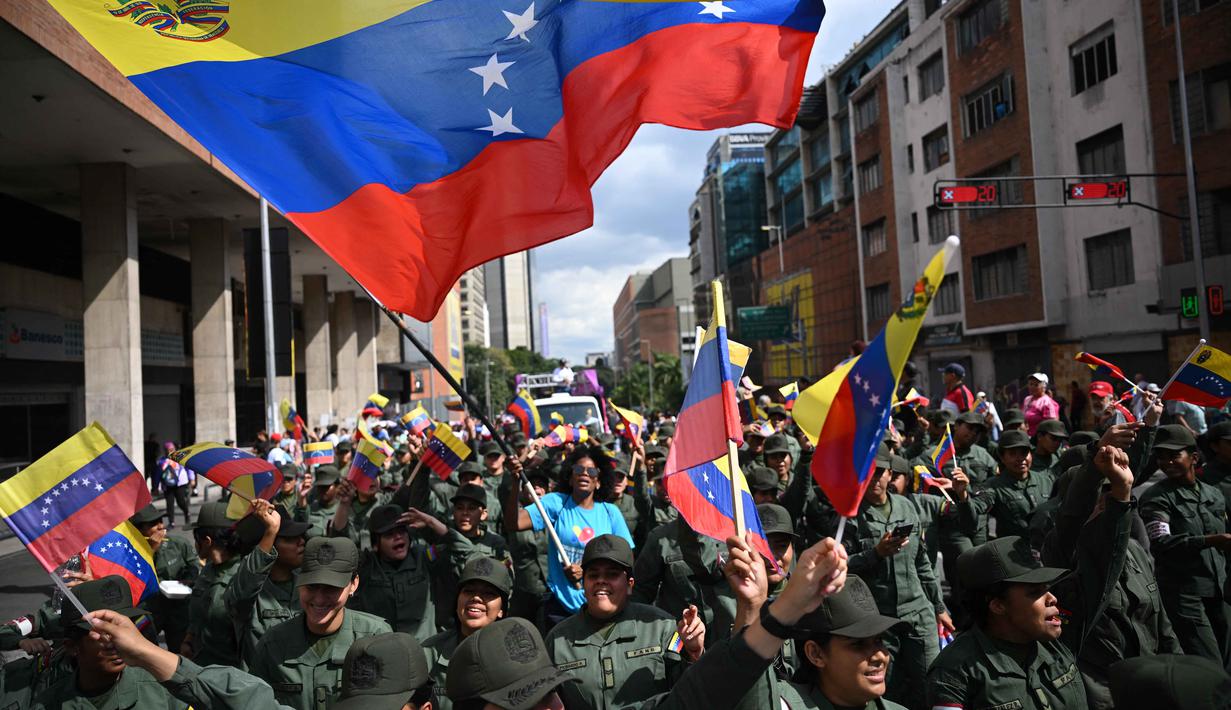 Penangkapan dilakukan atas perintah Presiden Amerika Serikat, Donald Trump, terkait tuduhan narkoterorisme, perdagangan narkoba internasional, dan penyelundupan kokain. Tampak dalam foto, seorang wanita mengibarkan bendera Venezuela di antara anggota Angkatan Bersenjata Bolivarian Nasional selama demonstrasi dukungan untuk mantan Presiden Venezuela Nicolas Maduro dan istrinya Cilia Flores di Caracas pada 6 Januari 2026. (Federico PARRA/AFP)