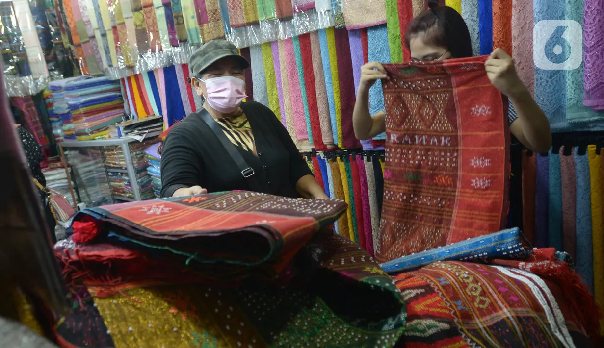 Pembeli melihat-lihat kain ulos di pasar proyek Senen, Jakarta, Kamis (21/10/2021). Sejak status PPKM turun menjadi level 2, pengunjung ramai mendatangi toko membeli kain ulos untuk upacara pernikahan adat dengan kisaran harga dari Rp. 500.000 hingga jutaan rupiah. (merdeka.com/Imam Buhori)