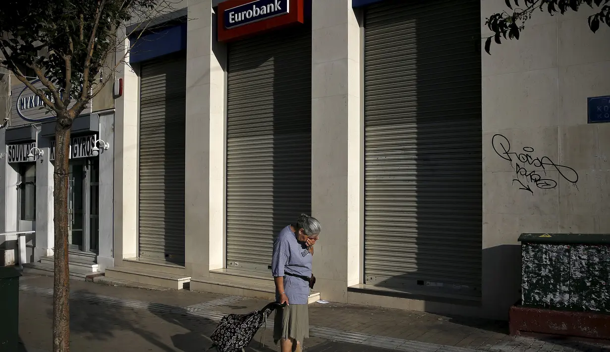 Seorang wanita melintas di depan sebuah bank yang berhenti beroperasi di Athena, Yunani, (29/6/2015). Seperti dikutip BBC, penarikan uang pun dibatasi hanya 60 euro per hari. (REUTERS/Alkis Konstantinidis)