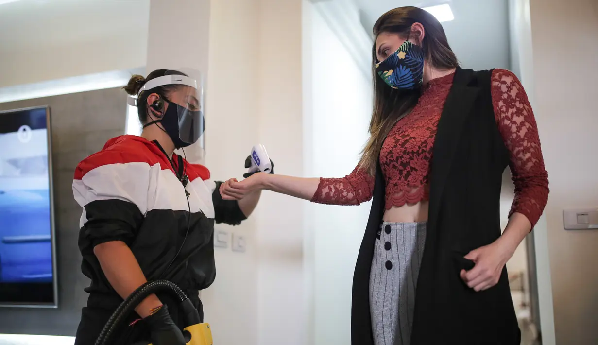 Seorang staf (kiri) memeriksa suhu tubuh tamu di hotel kapsul Caps Future Rooms, Bogota, Kolombia, 6 Agustus 2020. Sebagai respons terhadap COVID-19, hotel tersebut menerapkan sejumlah langkah keamanan dan sanitasi tambahan. (Xinhua/Jhon Paz)