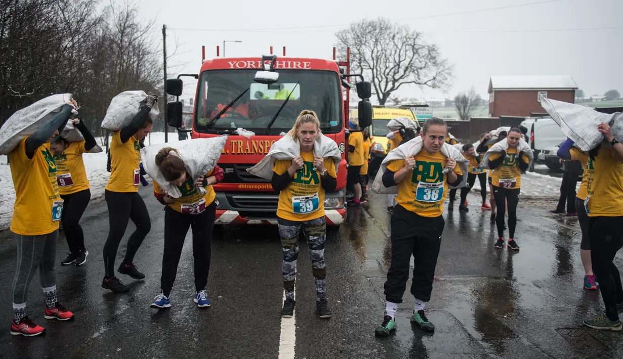 Peserta wanita membawa karung berisi batu bara saat mengikuti World Coal Carrying Championships di Desa Gawthorpe, Wakefield, Inggris Utara, Senin (2/4). Kompetisi  tahunan mengakut karung batu bara ini dalam memperingati Senin Paskah. (OLI SCARFF/AFP)