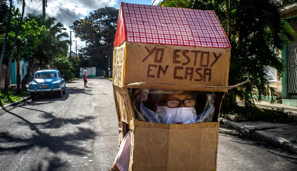 Feridia Rojas, seorang pensiunan perawat (82), memakai kotak kardus berbentuk rumah untuk melindungi dirinya dari penyebaran Covid-19 di Havana, Kuba, 8 Juli 2020. Pakaian pelindung kardus itu dipakai Rojas untuk melakukan aktivitas di luar rumah sehari-hari seperti berbelanja. (AP/Ramon Espinosa)