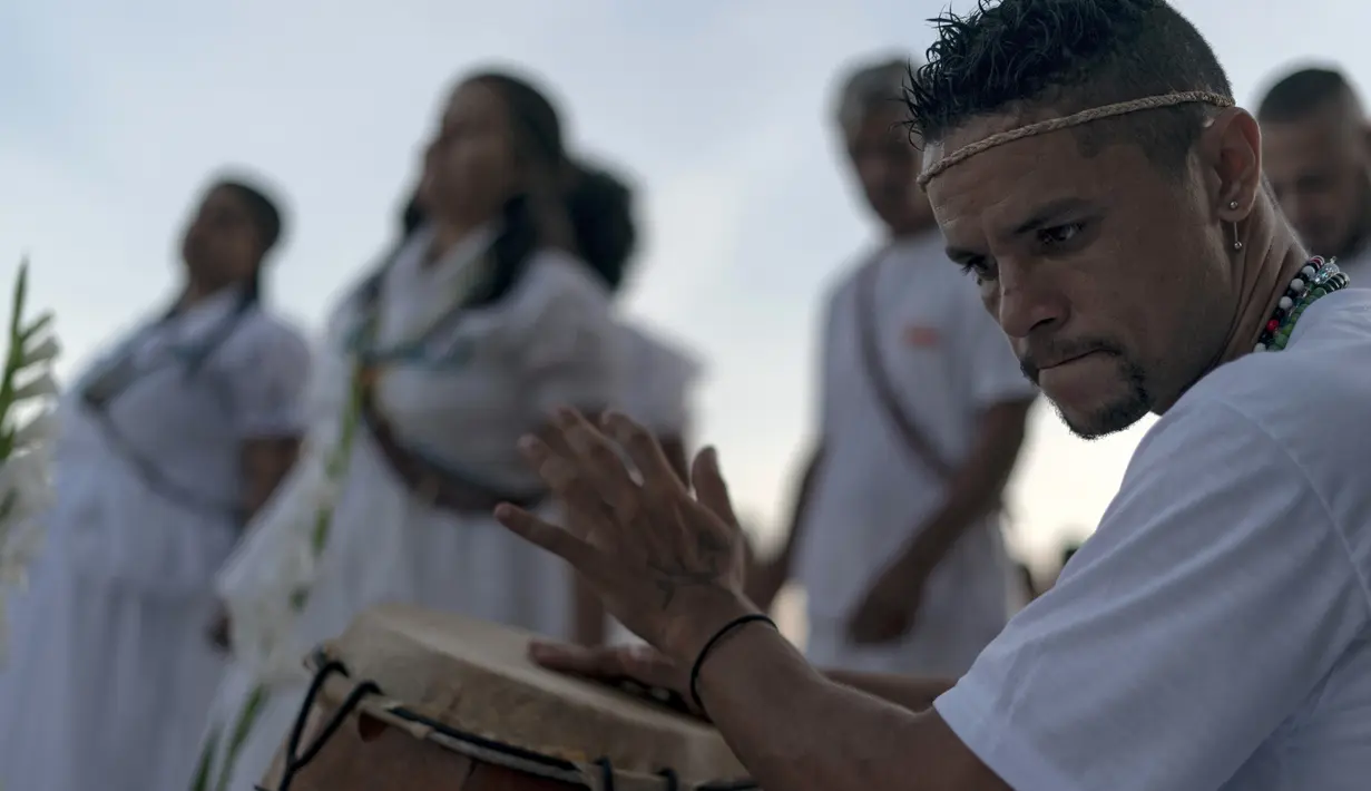 Seorang pria memainkan gendang saat memberi penghormatan kepada Yemenja sang Dewi Laut, ketika menyambut tahun baru di Pantai Copacabana di Rio de Janeiro (29/12/2019). Pengikut Yemanja melakukan ritual tersebut agar mendapat berkat di tahun yang akan datang. (AFP/Mauro Pimentel)
