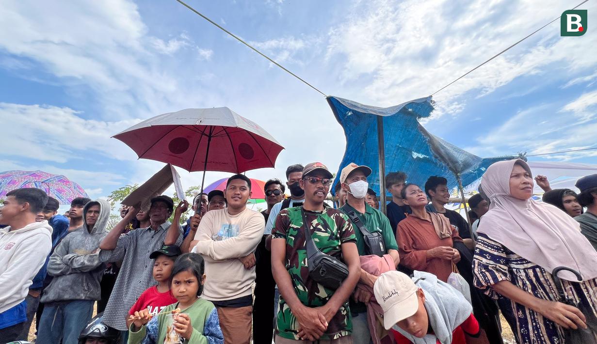 Warga yang hadir rela berpanas-panasan ketika suhu udara mencapai 36 derajat celsius. Demi melindungi kepala dari terik matahari, mereka menggunakan payung hingga spanduk. (Bola.com/M Iqbal Ichsan)