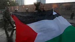 Seorang wanita membentangkan bendera Palestina saat unjuk rasa memprotes kebijakan Presiden AS, Donald Trump soal Yerusalem sebagai ibu kota Israel di luar Kedubes AS di Santiago, Chile, (11/12). (AP Photo / Luis Hidalgo)